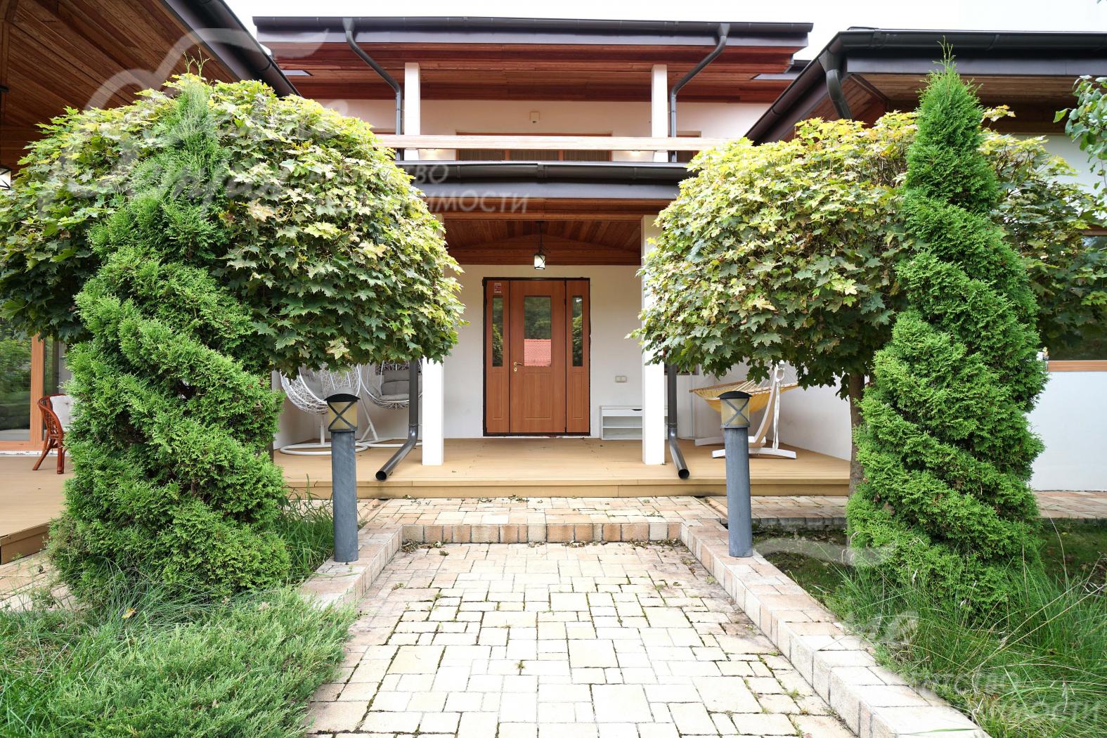 Главный вход в дом, украшенный декоративной подсветкой, клёнами и спиральными туями