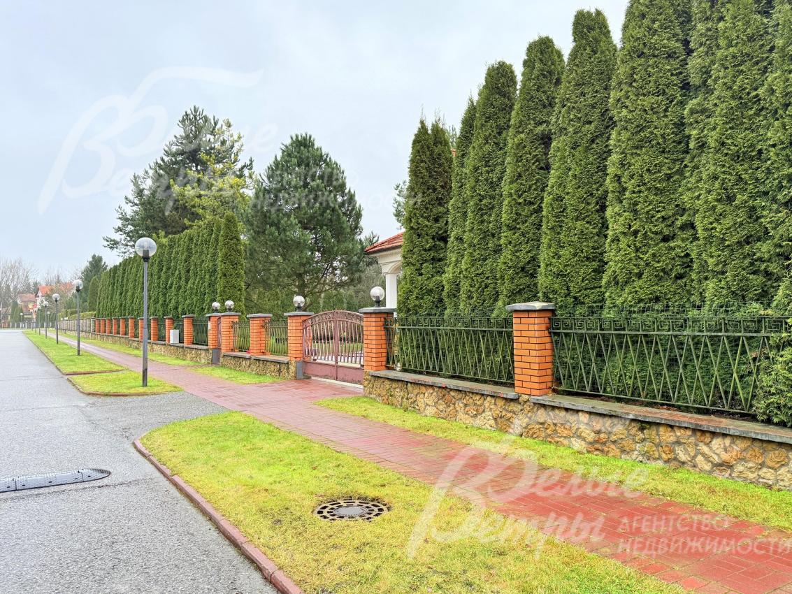 За оградой участка возвышается плотная живая изгородь из высоких ухоженных сосен. Деревья высажены ровными рядами, создавая эффект «зелёной стены» - это не только красиво выглядит, но и обеспечивает приватность территории