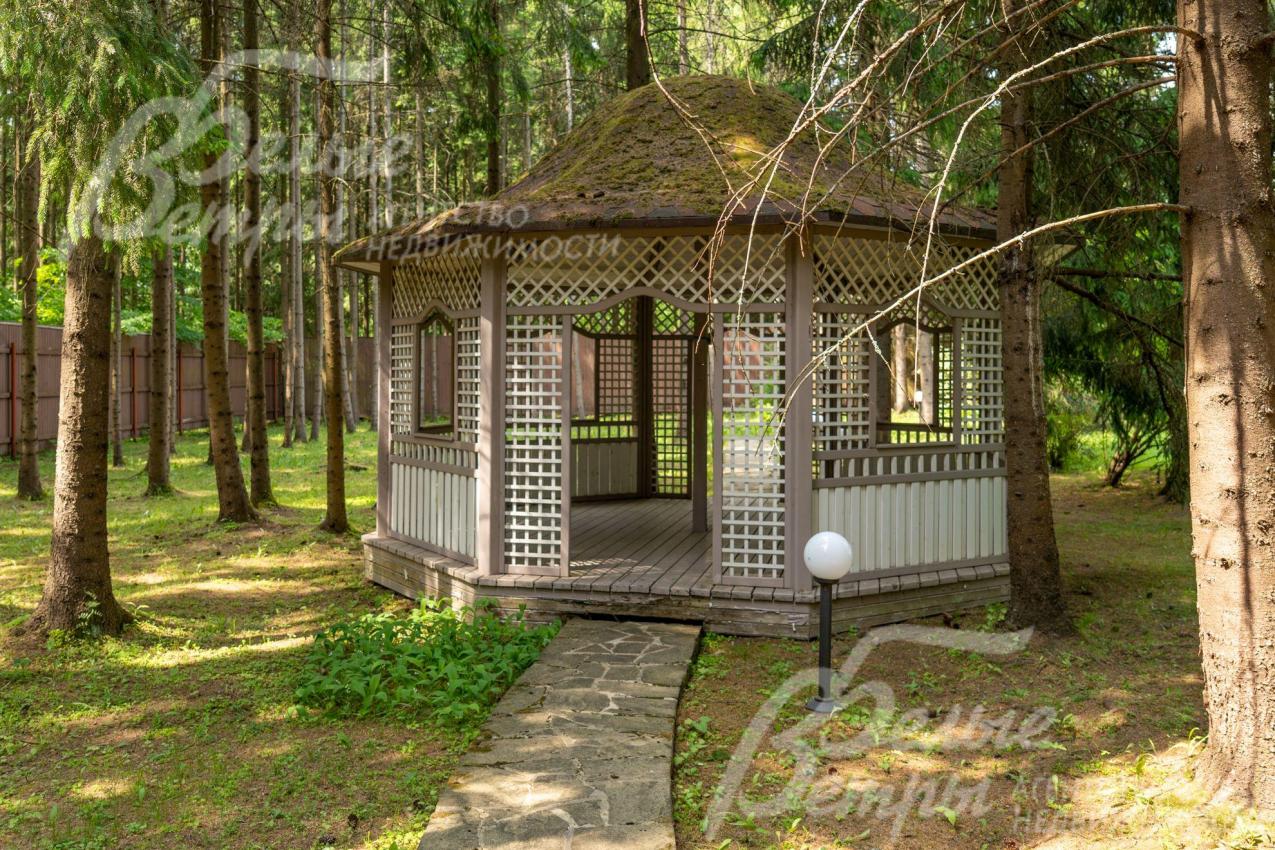 Еще одна изящная деревянная беседка в тени лесных деревьев.