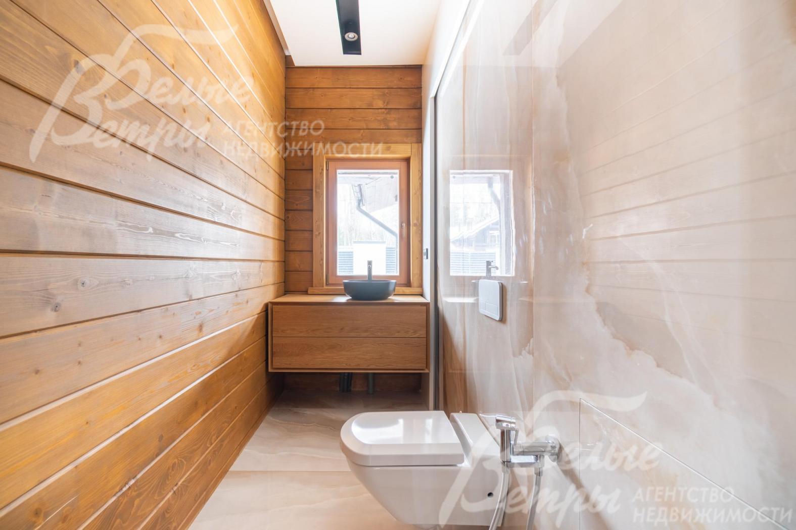 Санузел на первом этаже. Стены облицованы деревянными панелями и крупной светлой плиткой с мраморным рисунком