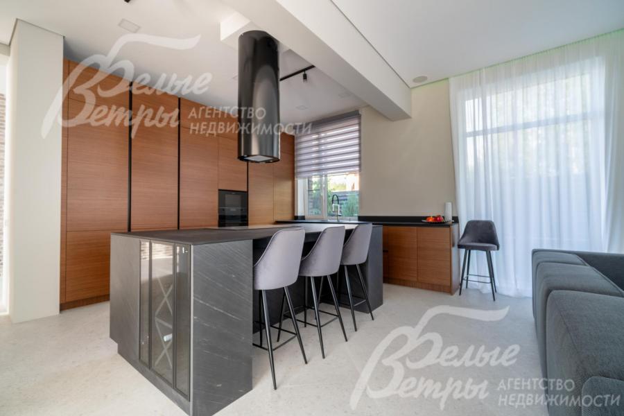 На кухне установлен гарнитур с фасадами из шпона ореха и остров с полубарным столом