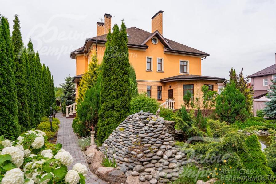 На участке альпийская горка, множество хвойных деревьев и цветущих растений