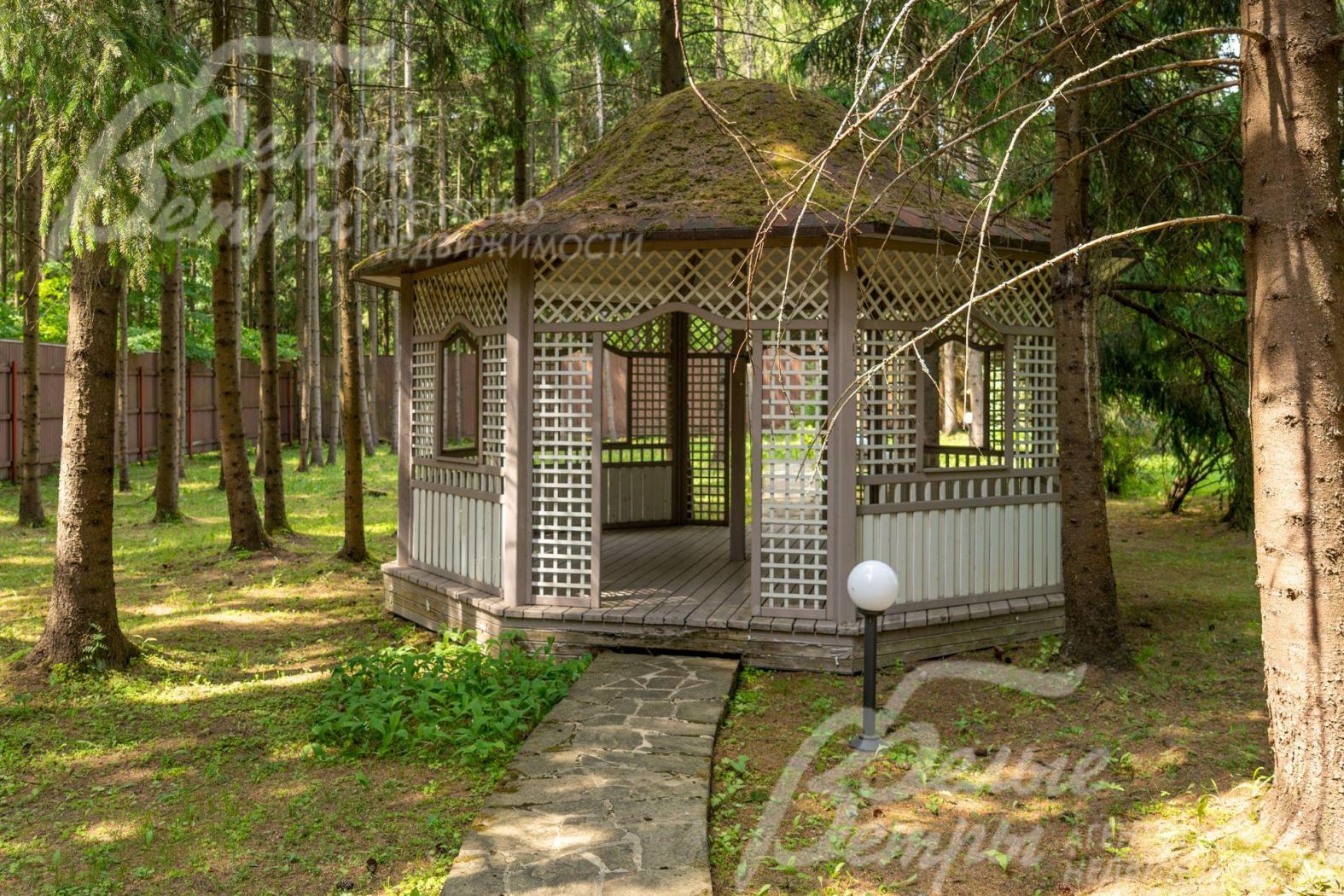Еще одна изящная деревянная беседка в тени лесных деревьев.